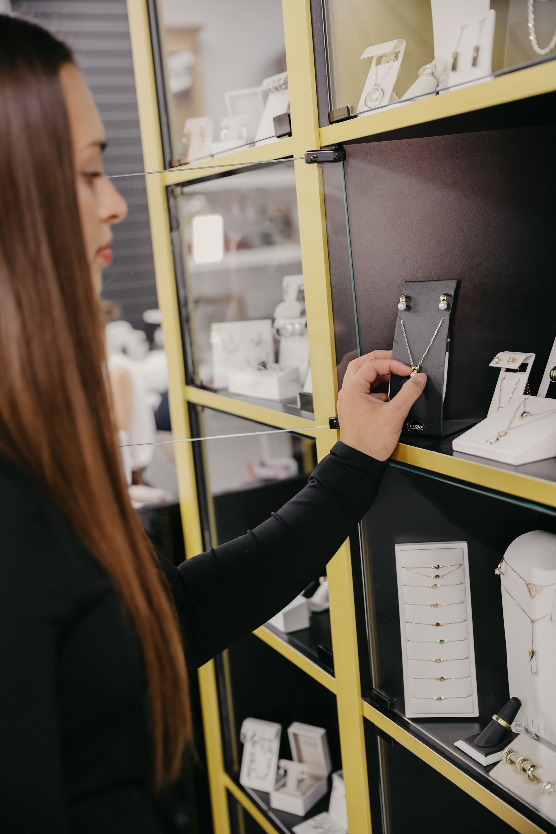Une femme vêtue de noir examine un collier exposé dans une bijouterie.