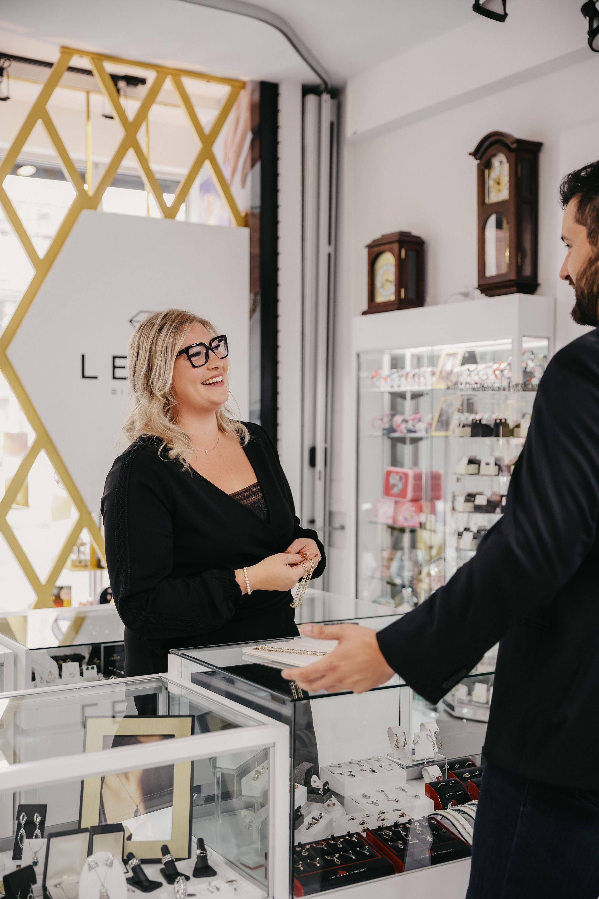 Une femme portant des lunettes parle à une cliente au comptoir d'une bijouterie.