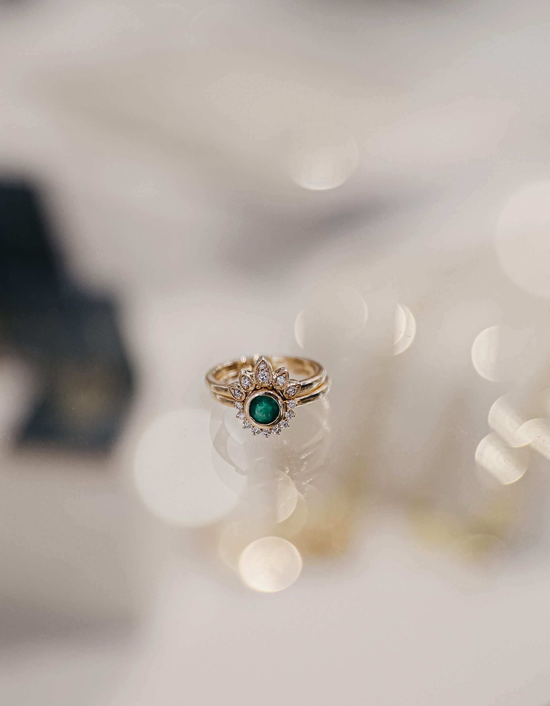 Bague en or ornée d'une pierre précieuse verte, entourée de diamants, sur une surface réfléchissante.