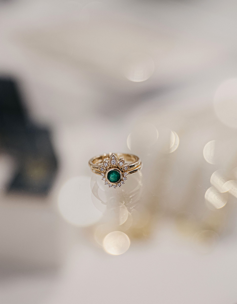 Bague en or ornée d'une pierre précieuse verte, entourée de diamants, sur une surface réfléchissante.