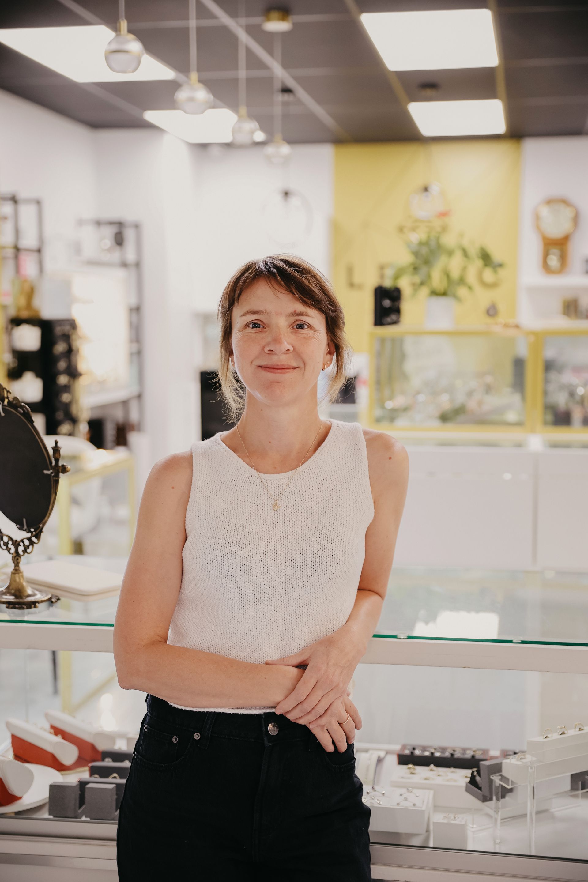 Une femme en haut blanc et pantalon noir sourit dans une bijouterie.