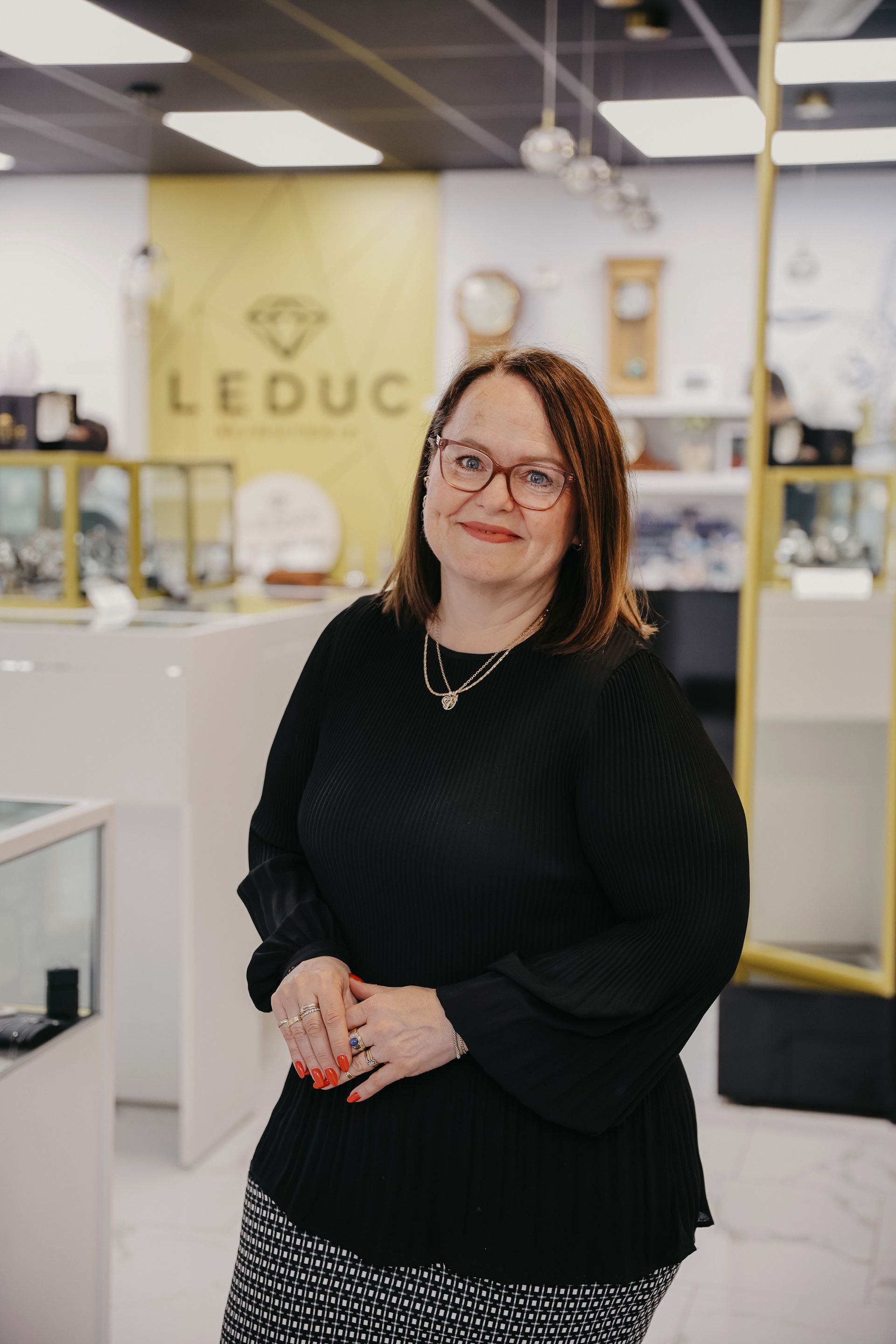 Femme dans une bijouterie, portant des lunettes et un pull noir.