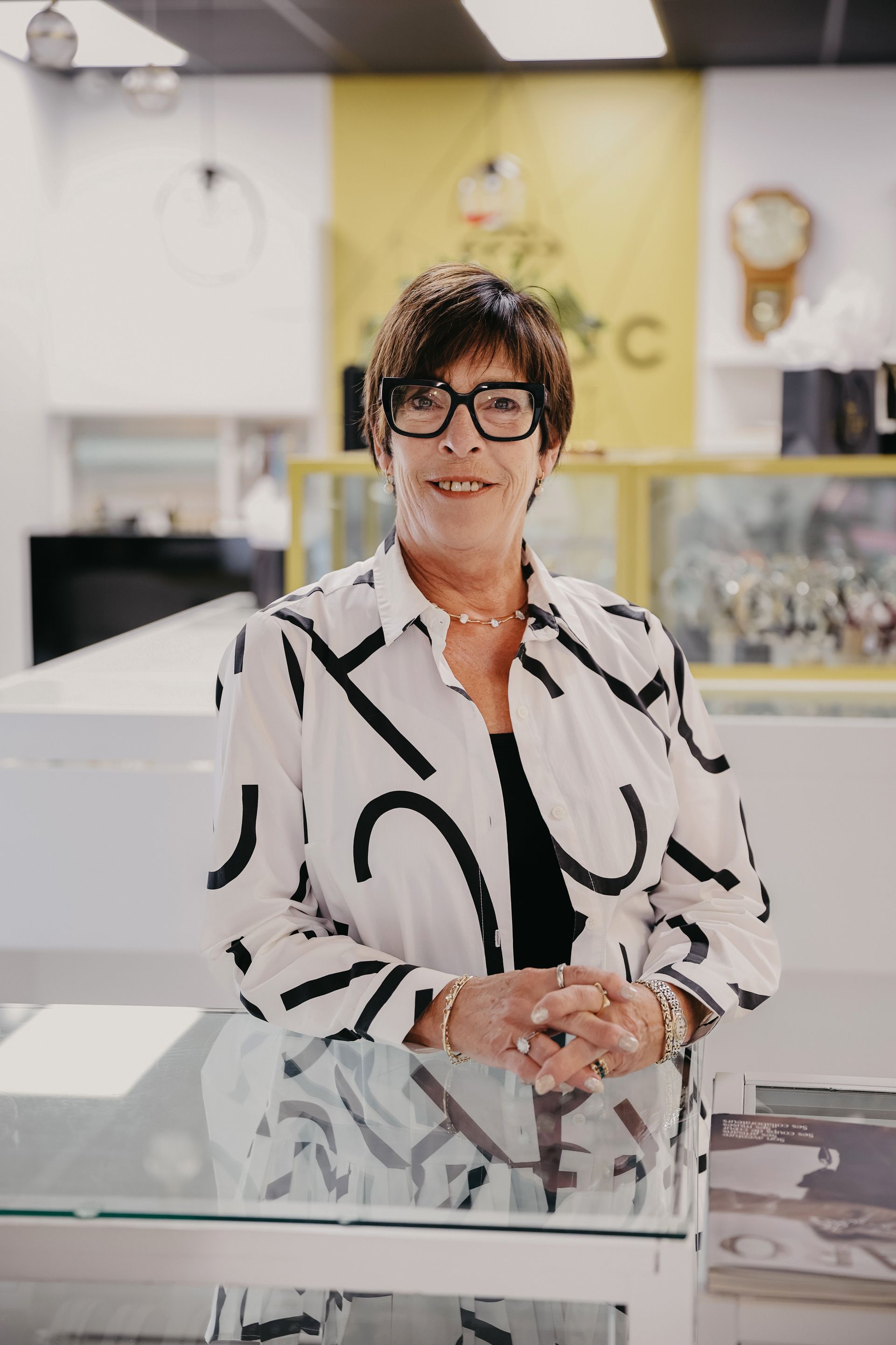Une femme portant des lunettes et une chemise à motifs se tient dans une bijouterie.