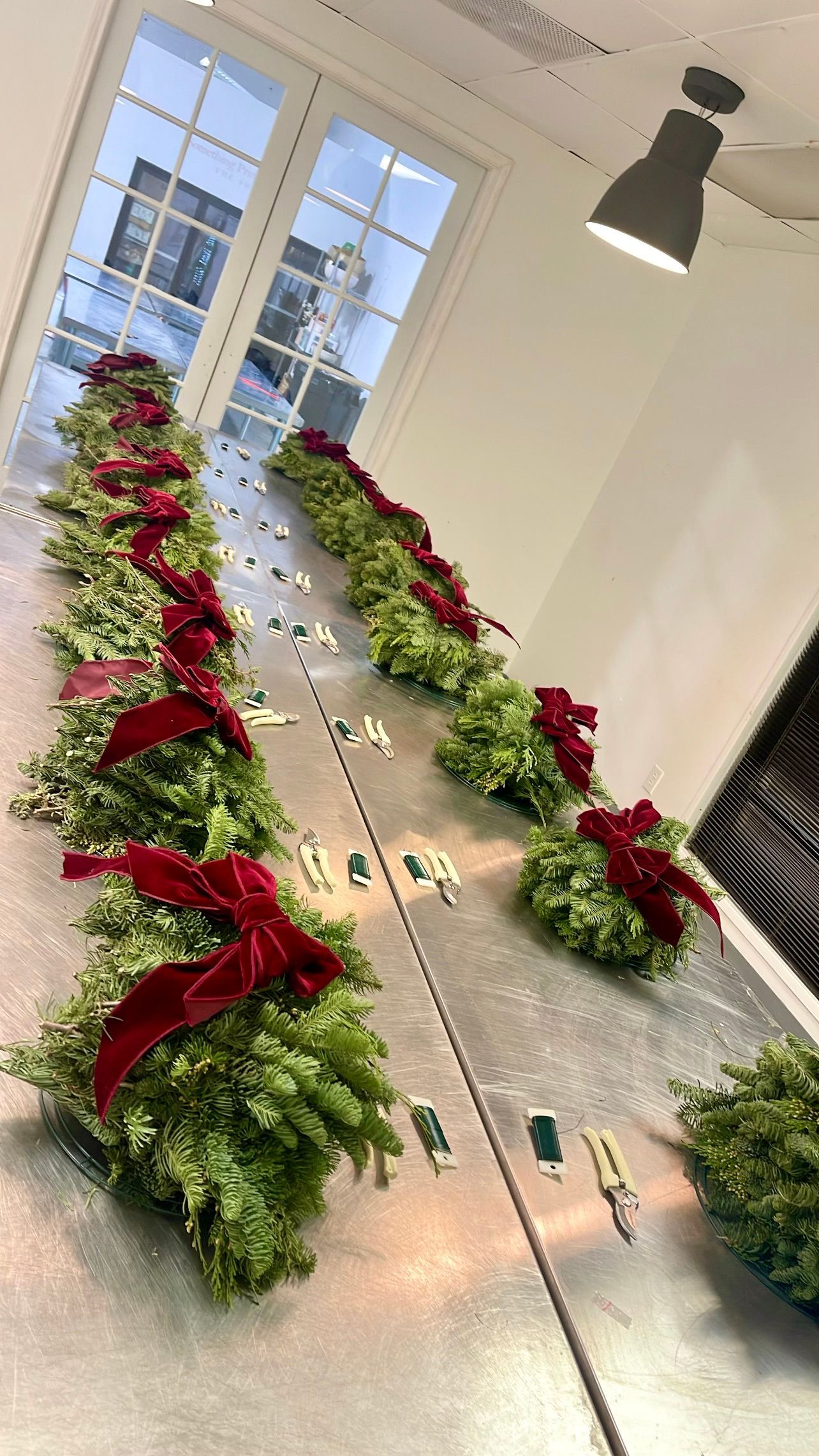 Long table decorated with evergreen wreaths and red velvet bows for Christmas, in a bright room.