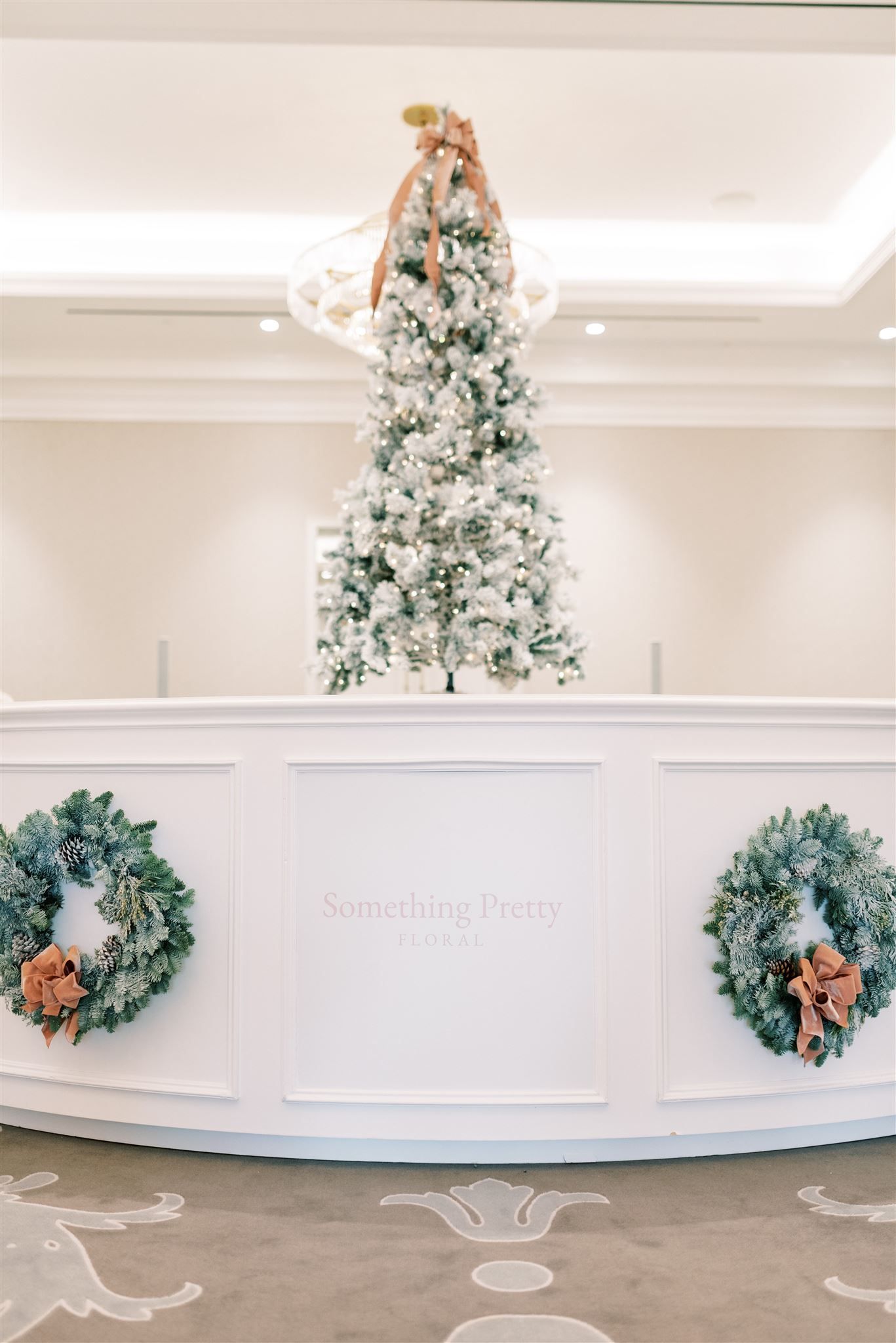 White hotel reception desk with wreaths, a snow-covered Christmas tree, and gold accents.