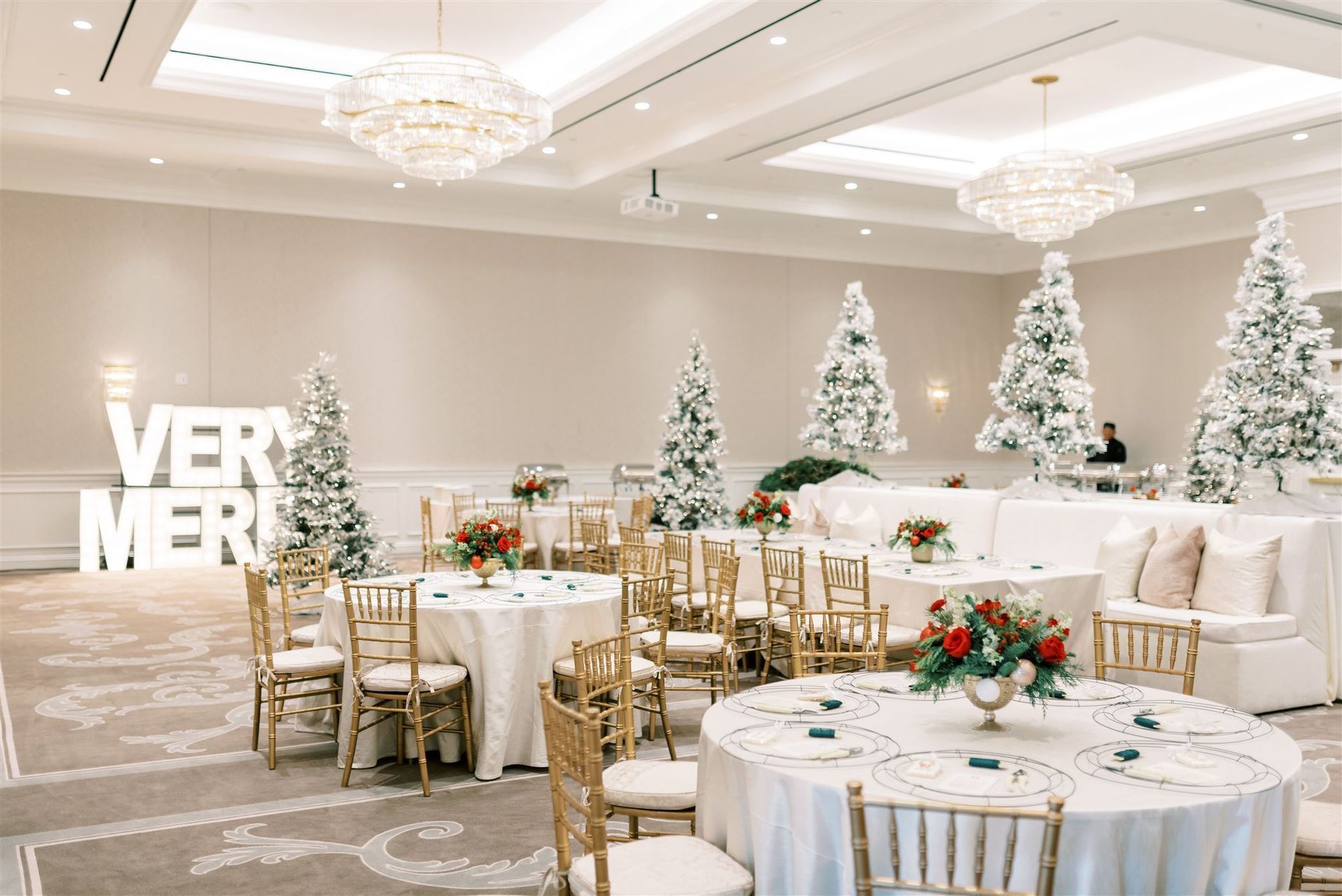 Elegant Christmas event: round tables, gold chairs, white flocked trees, floral centerpieces, and 