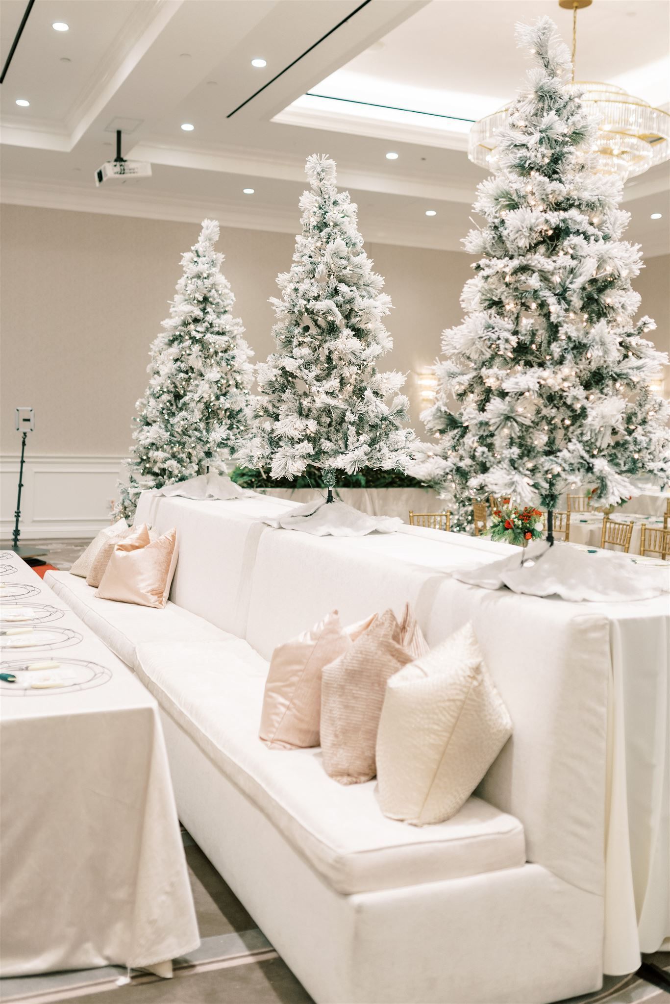 White couch with pink pillows in front of snow-covered Christmas trees in a bright room.