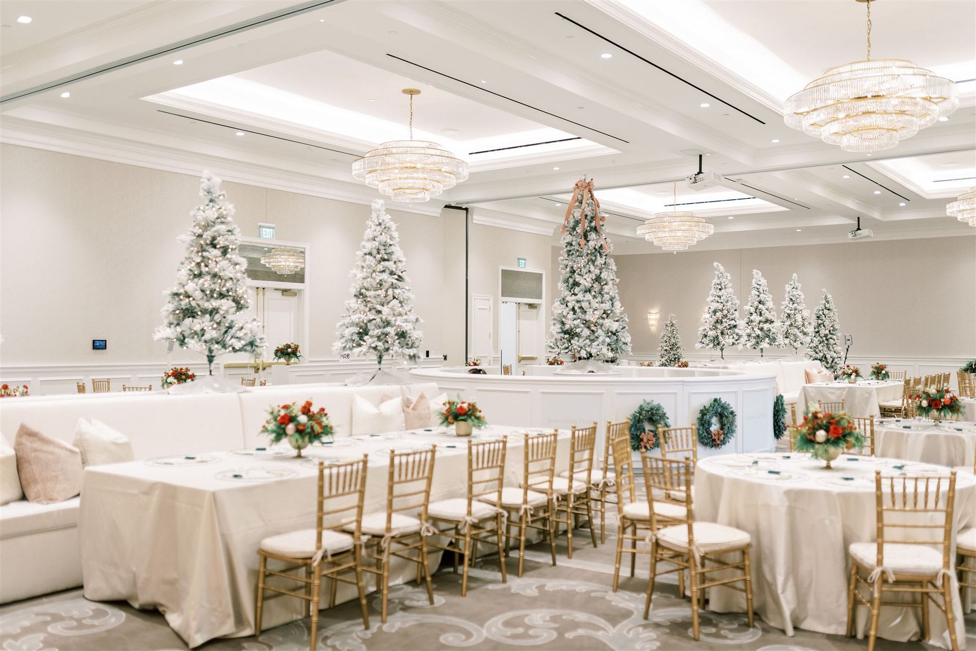 Elegant ballroom decorated for Christmas, with snow-covered trees, gold chairs, and tables set for a holiday event.