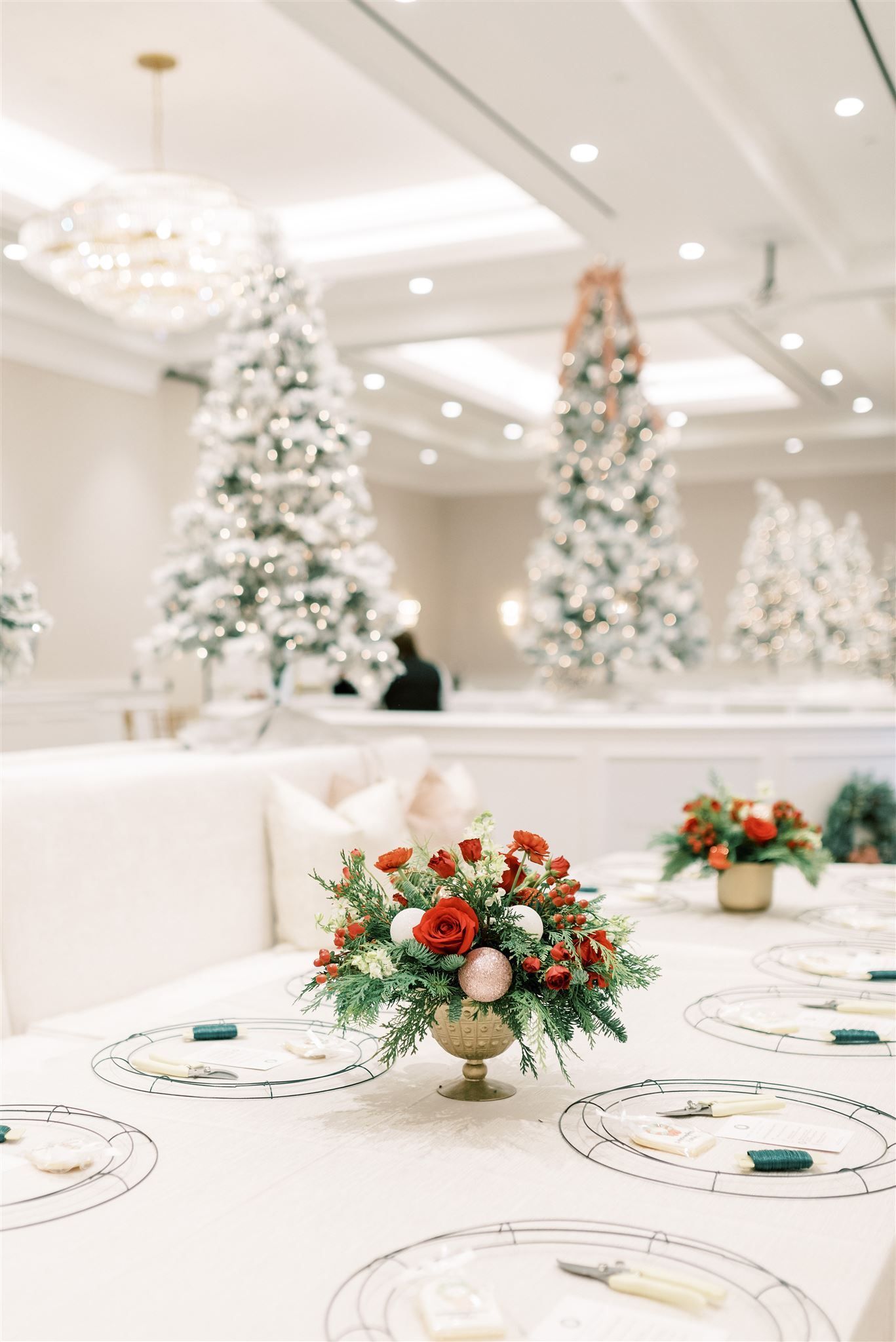 Formal dining table set for Christmas; flower arrangements, snowy trees in the background.