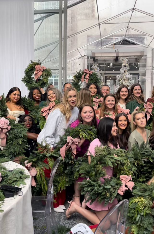 Group of women with Christmas wreaths posing in a bright indoor setting.