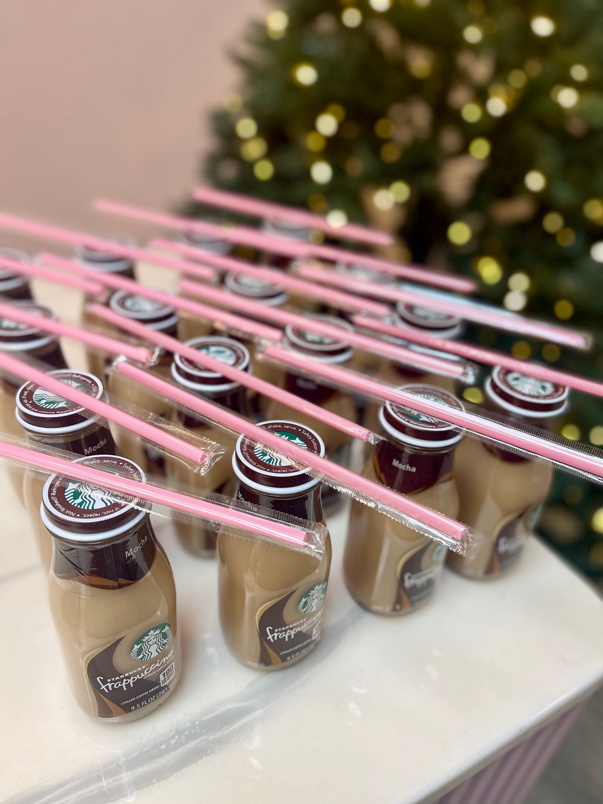 Starbucks Frappuccino bottles with pink straws, arranged on a table in front of a Christmas tree.