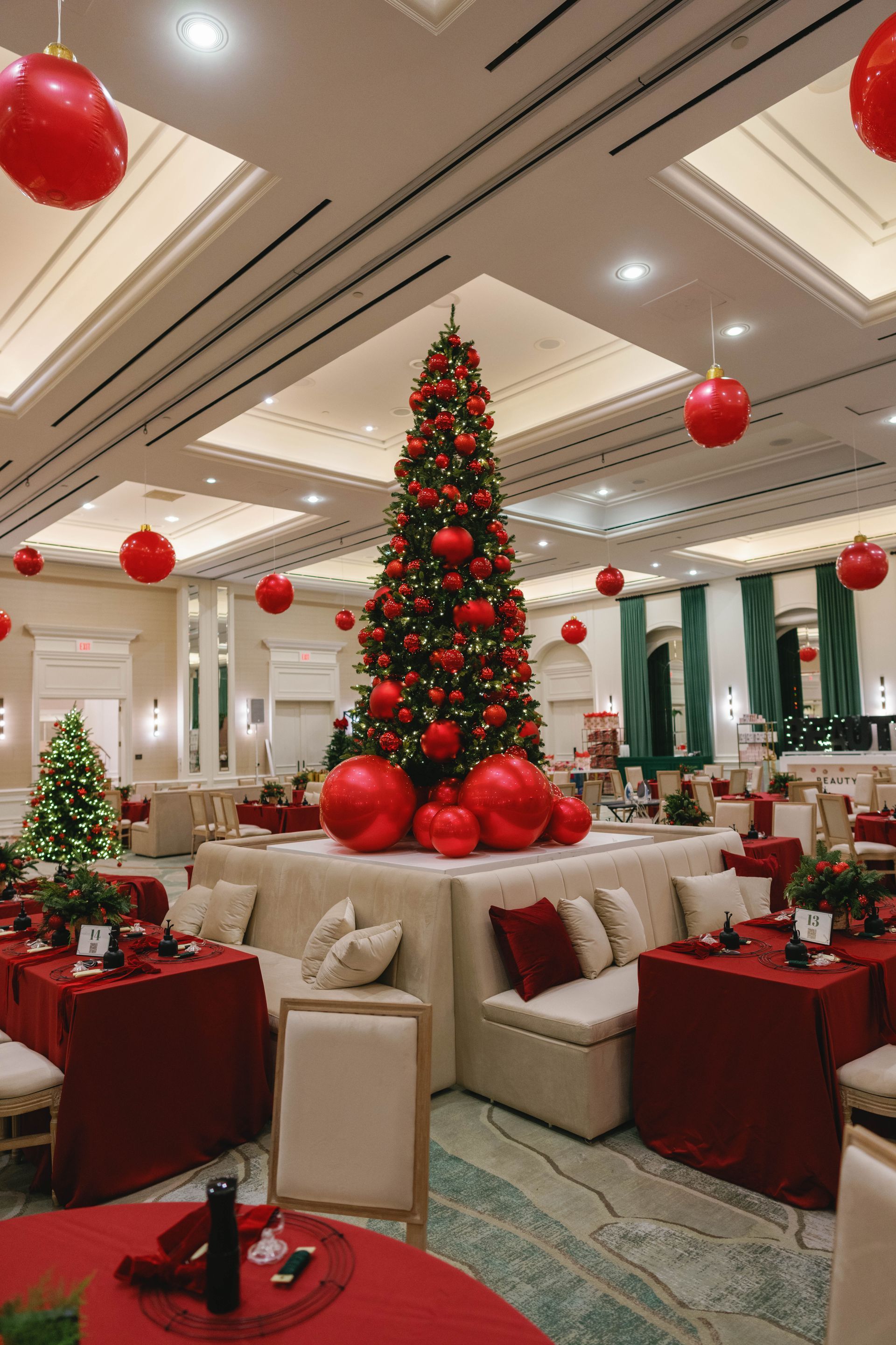 Festive dining room with tall Christmas tree, red ornaments, and tables with red tablecloths.