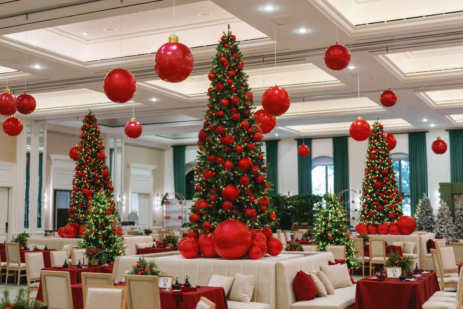 Christmas-decorated ballroom with several lit trees, red ornaments, and seating arrangements.