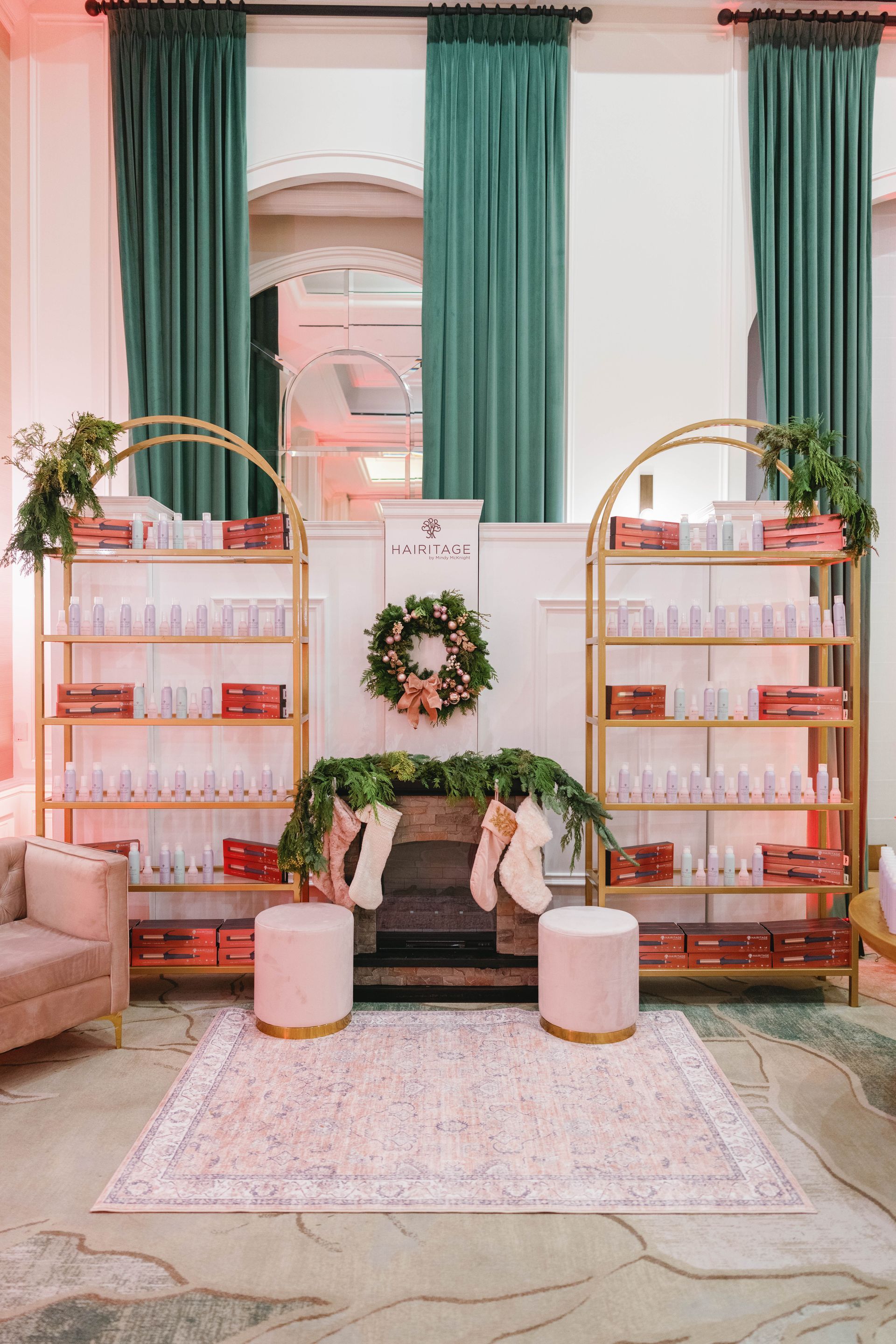 A decorated display for products. Gold shelves, pink seats, and a fireplace with a wreath, against green curtains.