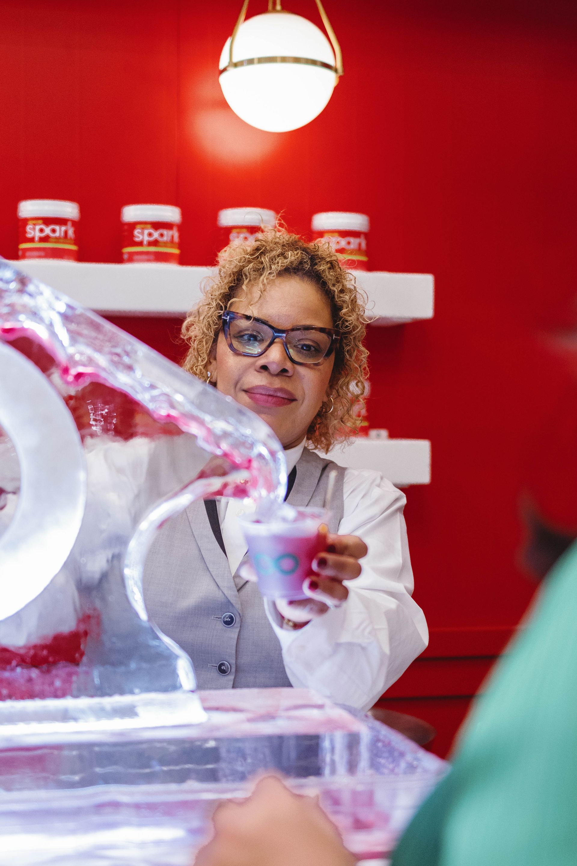 Woman in glasses pouring red drink into glass at ice bar. Red wall and 