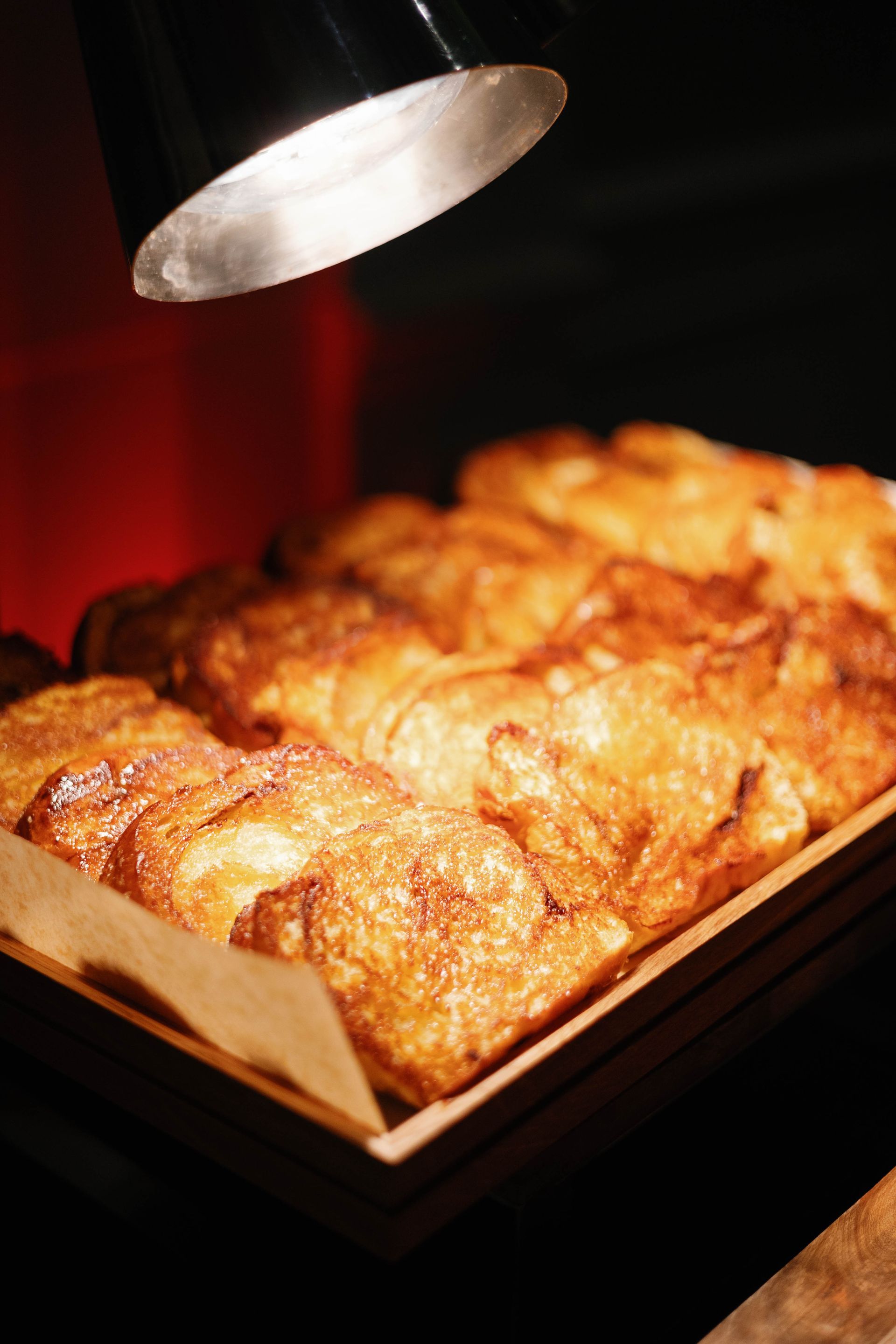 Golden-brown pastries in a wooden tray, lit by a lamp.