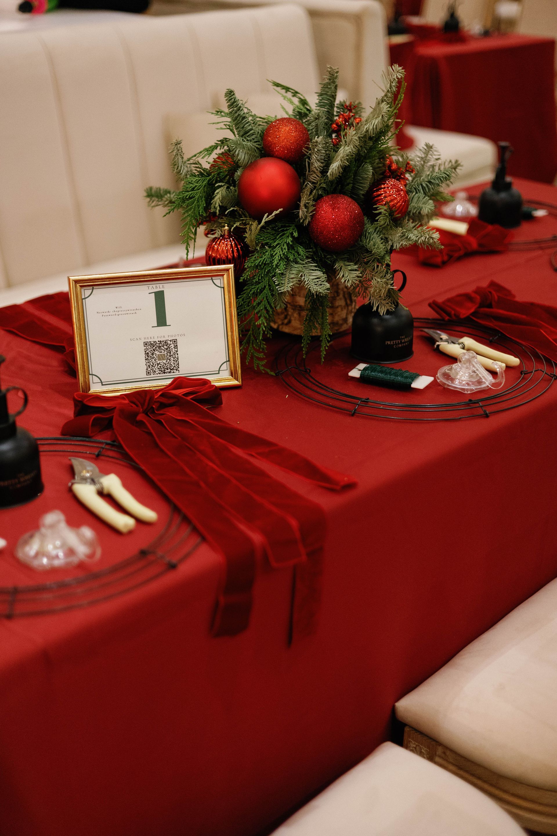 Christmas table setting with red cloth, floral arrangement, and craft supplies.
