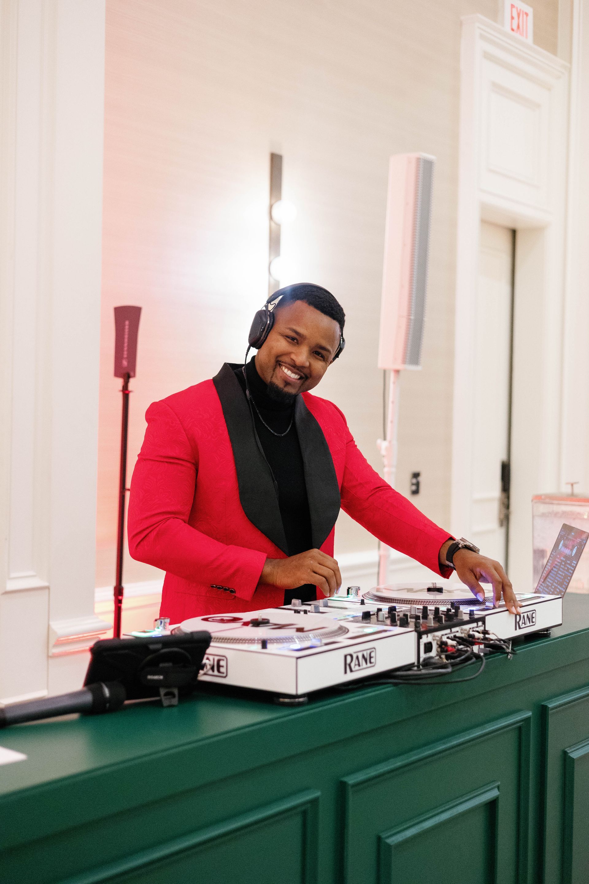DJ in red jacket and headphones at a green bar.