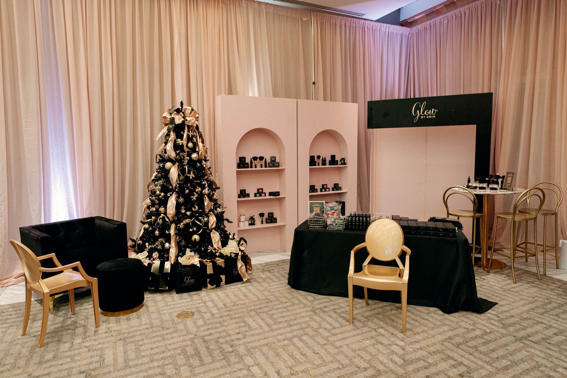 A luxurious event space with a Christmas tree, perfume display, seating, and a black and pink color scheme.