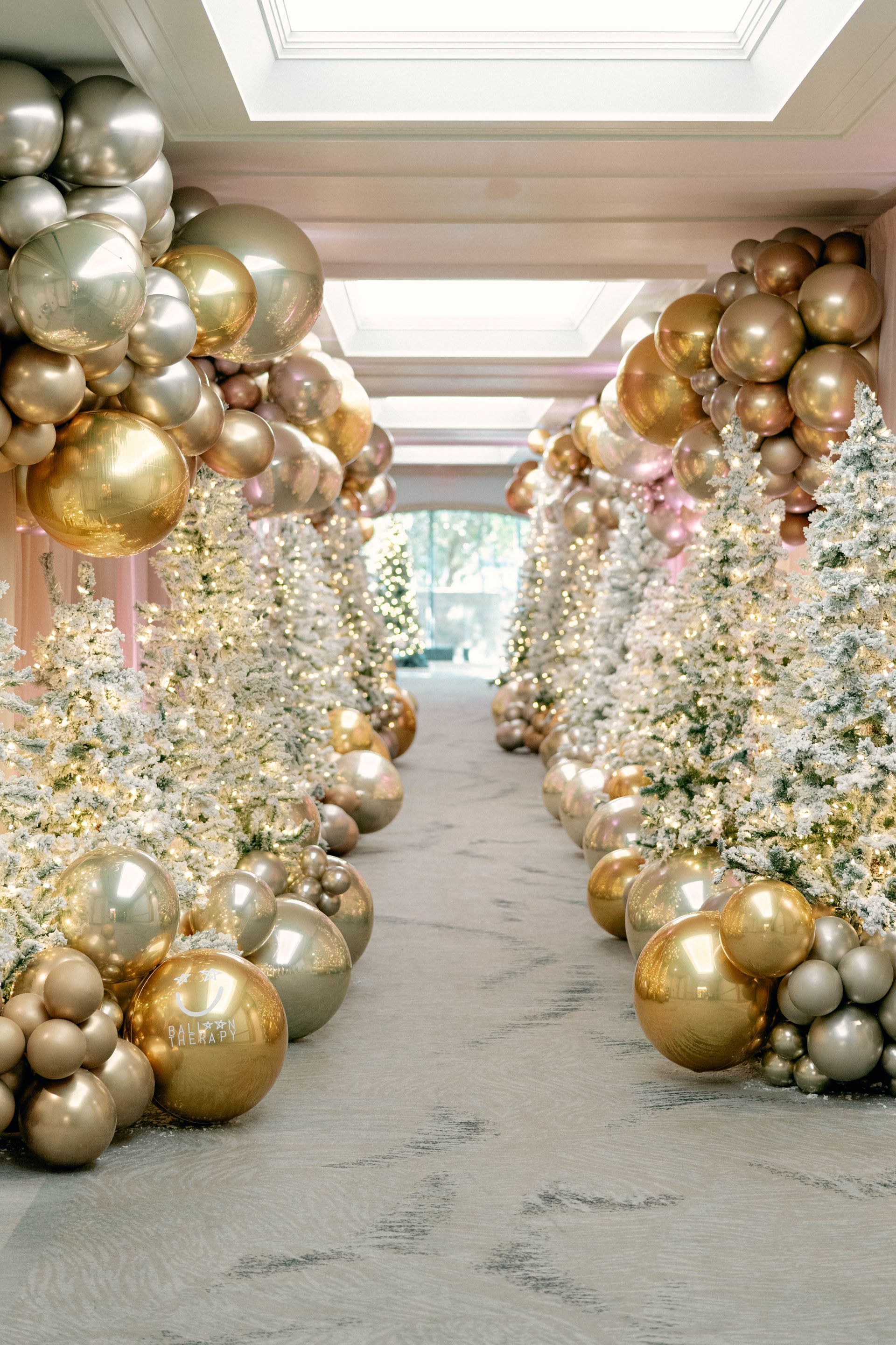 Gold and silver balloons and frosted Christmas trees line a hallway.