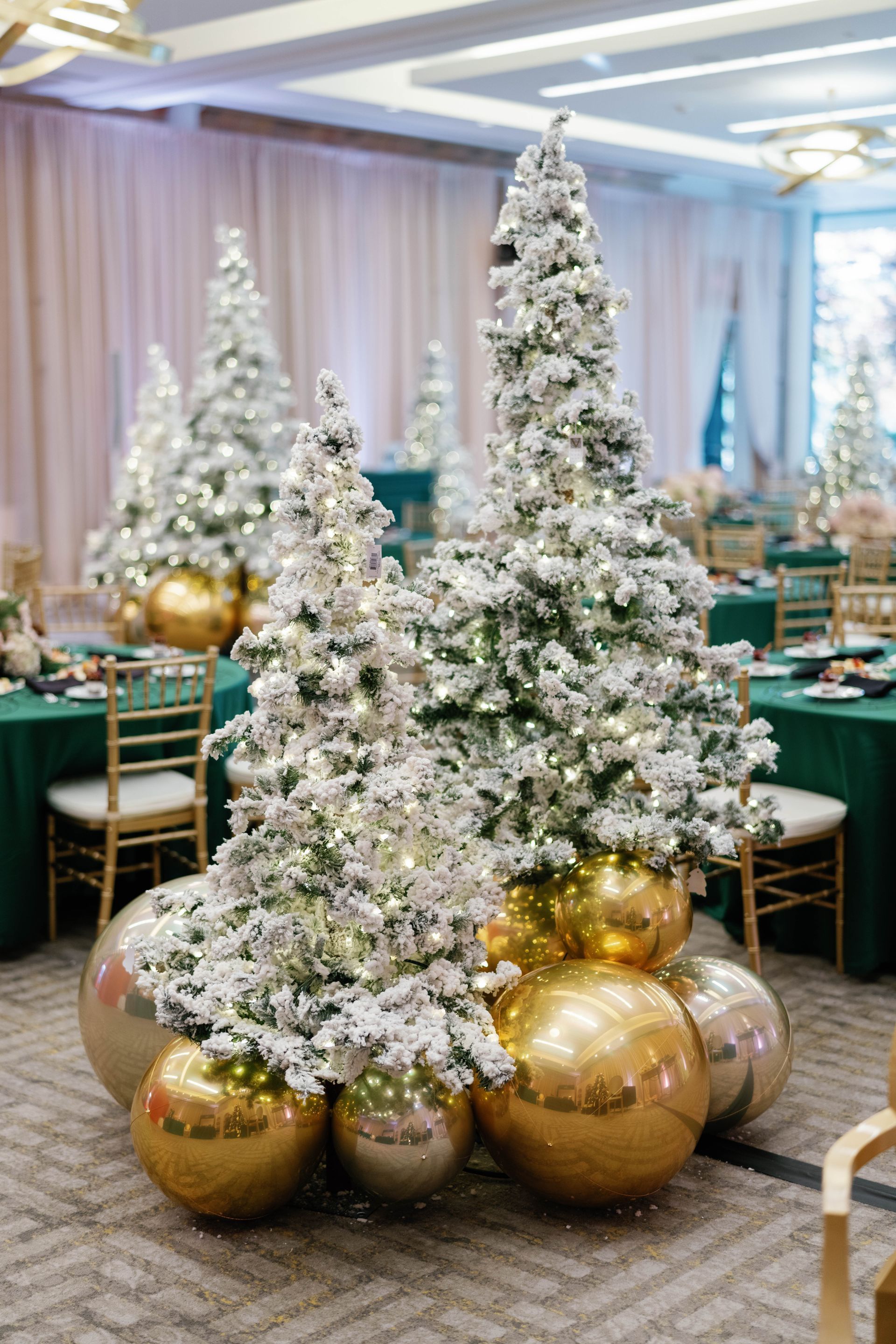 Flocked Christmas trees on gold and silver spheres, set in a dining hall with emerald green tablecloths.