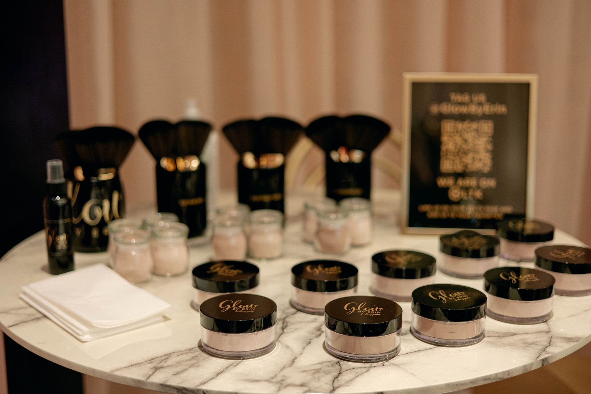 Makeup display on a round table with powder, brushes, and a sign.