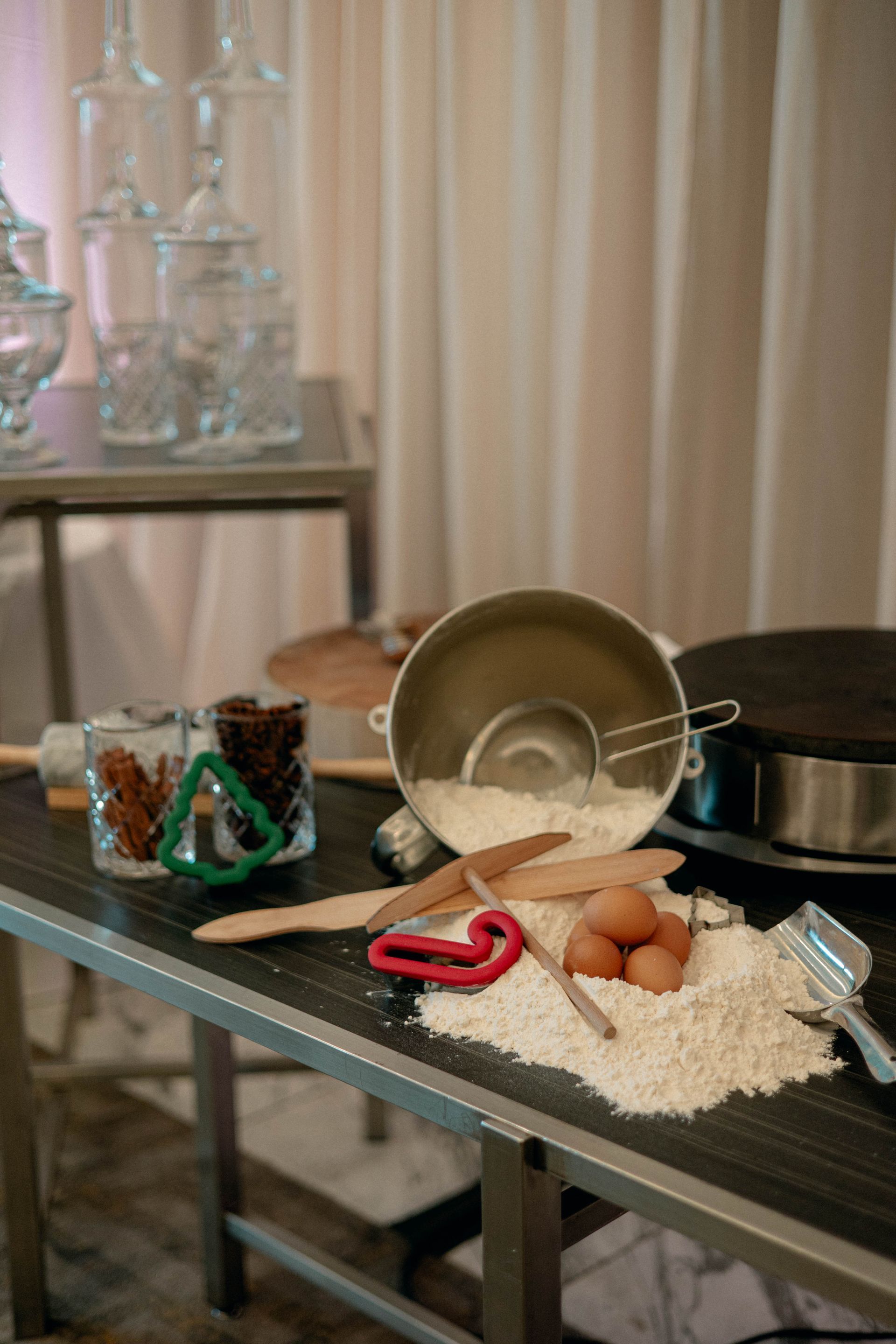 Baking scene: Flour, eggs, and utensils on a table, alongside cookies, a bowl, and a backdrop.
