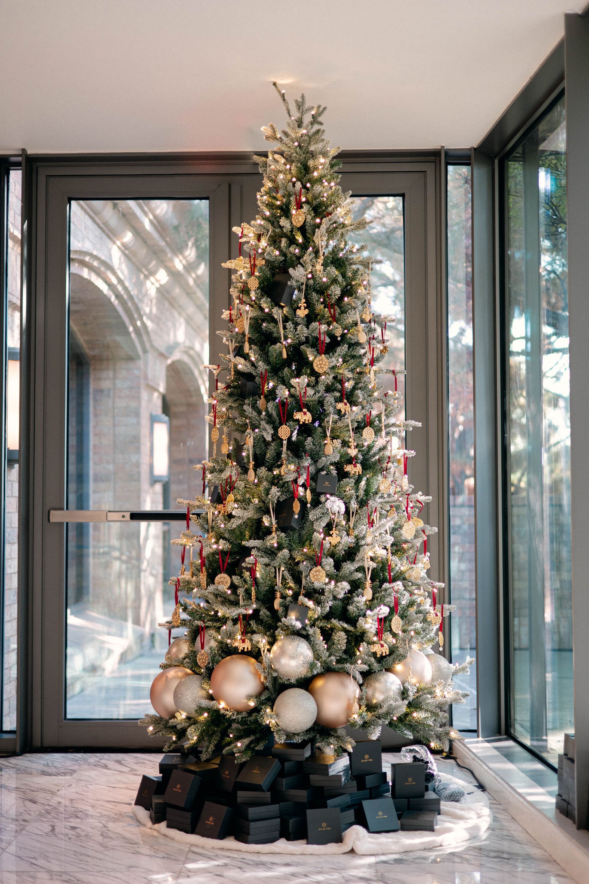 Christmas tree with ornaments and gifts, indoors with glass doors.