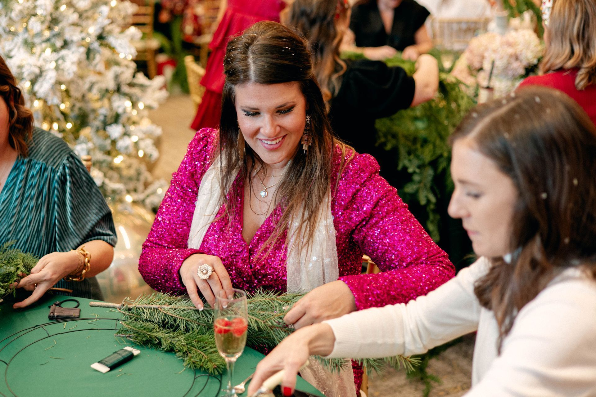 Woman in pink sequin jacket making a wreath at a festive gathering.