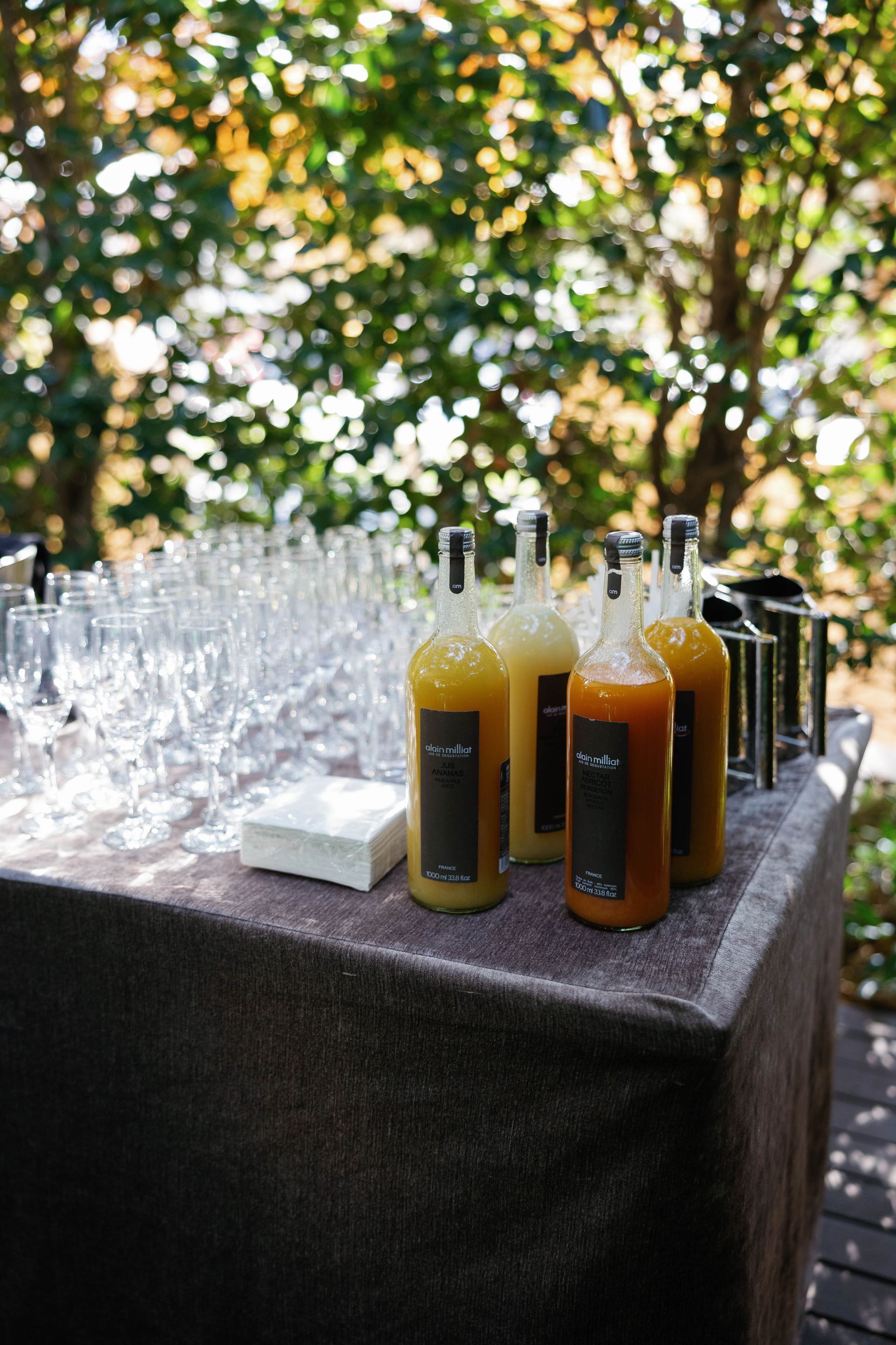 Bottles of juice on a table, glasses and napkins to the side, outdoors.