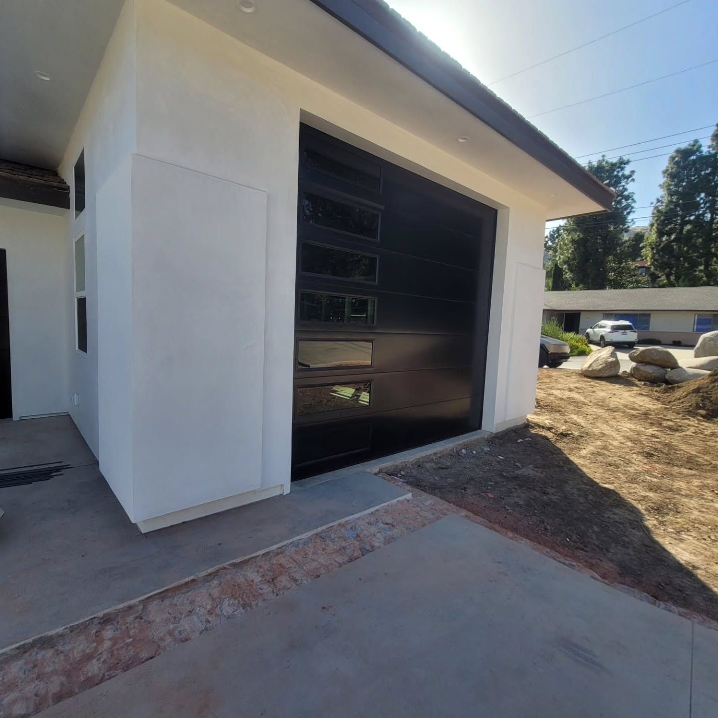 Modern white building with a large dark garage door and a concrete driveway beside a sloped yard