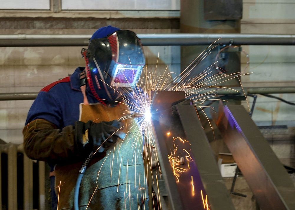 Welder in blue protective gear sparks metal fabrication indoors