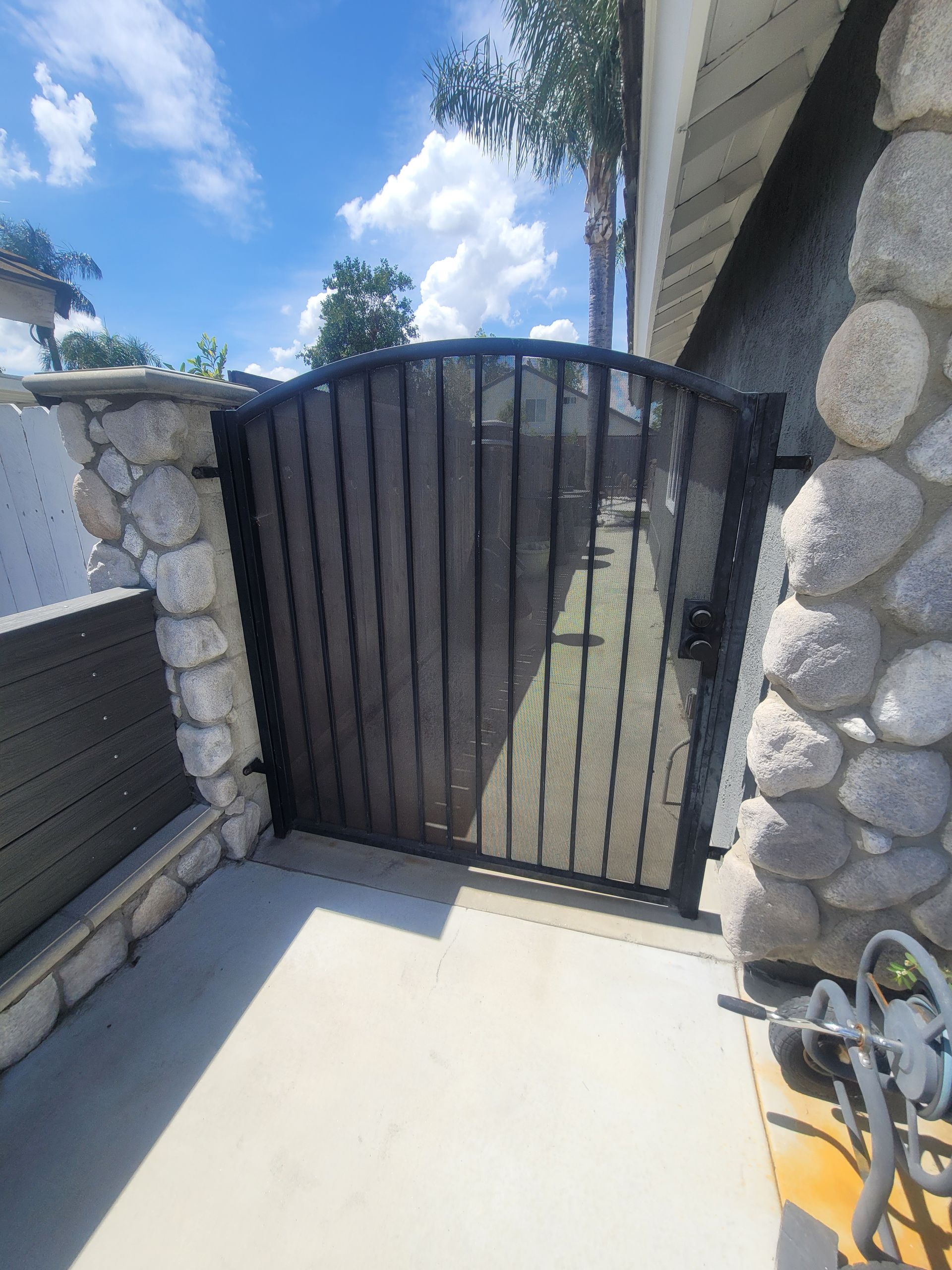 Black metal gate between stone walls at a sunlit outdoor walkway