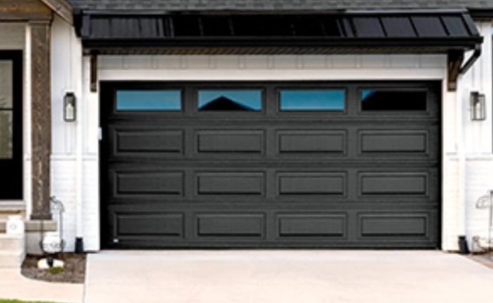 Dark gray garage door with three small blue windows under a black awning on a house exterior