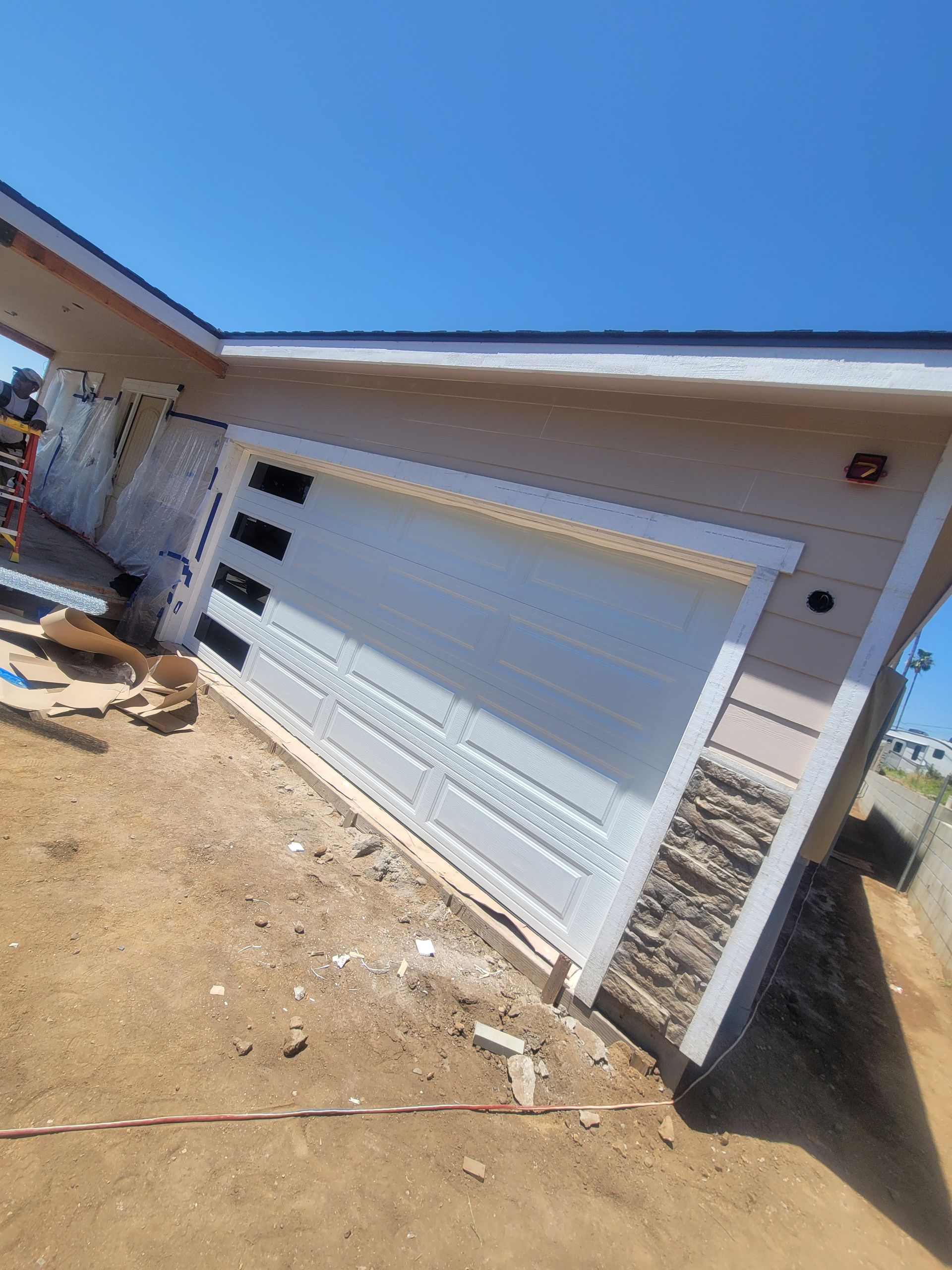 Tilted view of a white garage door on a brick house under a blue sky, with dirt yard in front