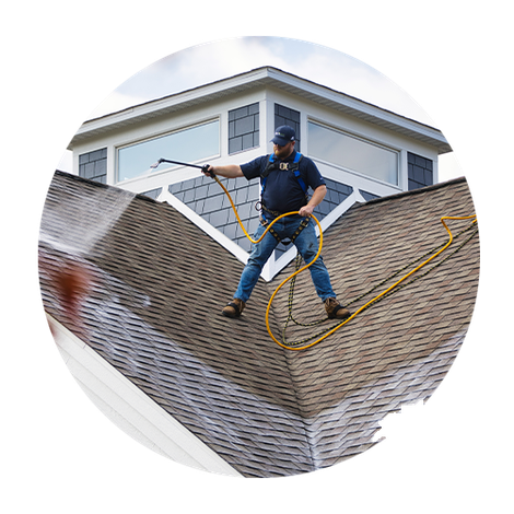Worker pressure-washing a roof with a hose and safety harness