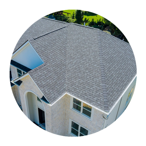 Aerial view of a house with a gray shingle roof and white exterior surrounded by trees