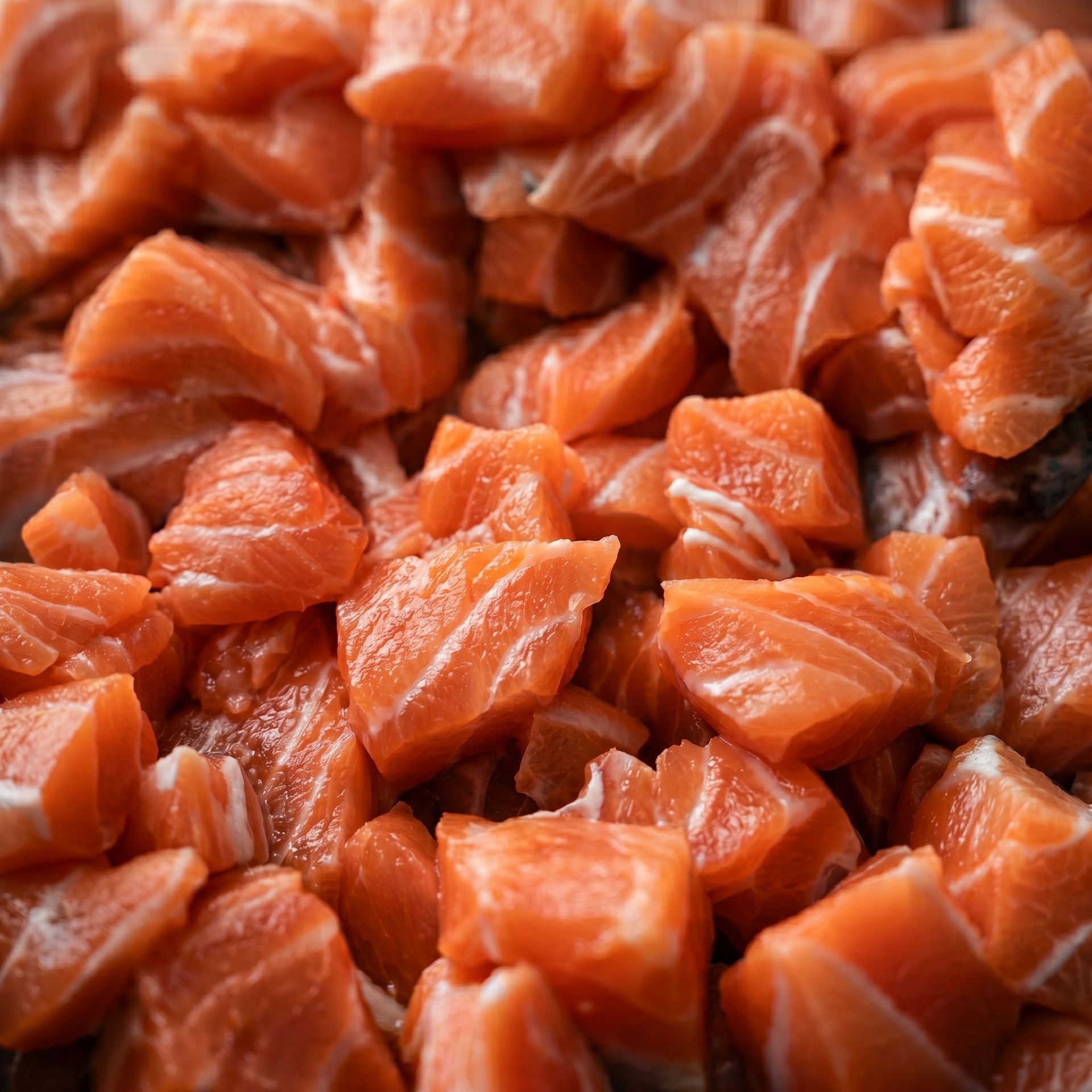 Close-up of diced raw salmon pieces, bright orange and glossy, filling the frame