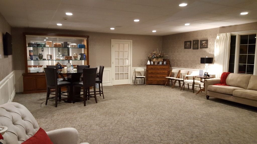 Spacious room with seating areas, a display cabinet, and a round table with chairs. Soft lighting, neutral colors.