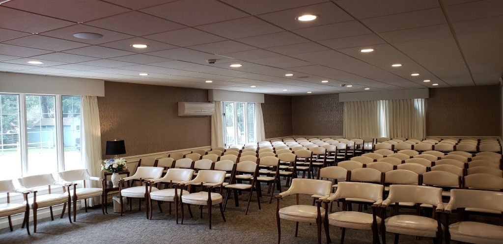 An empty conference room with rows of chairs, windows, and ceiling lights.