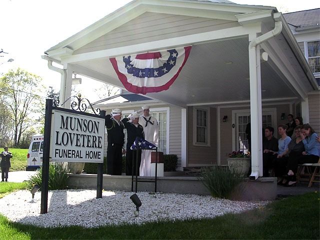 Funeral home, Munson Lovetere, with flag ceremony on porch. People in attendance and an American flag.