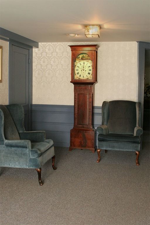 Two blue armchairs flank a grandfather clock in a room with patterned wallpaper and gray trim.