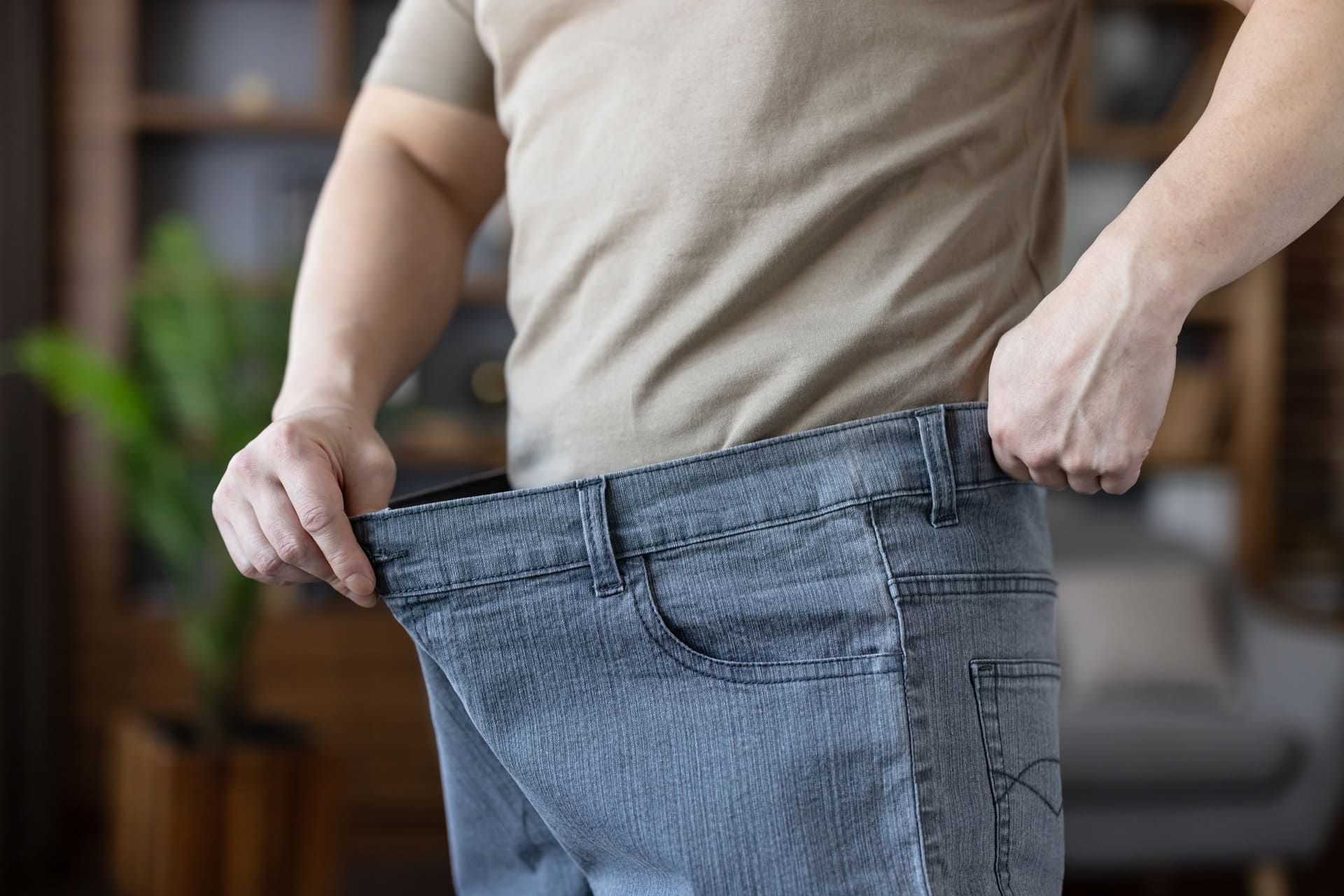 Man demonstrating successful weight loss and health transformation, holding out the waist of his loose, oversized jeans, symbolizing achievement in diet and fitness
