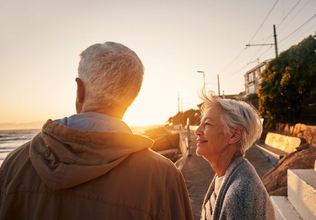 An elderly couple is walking on the beach at sunset.