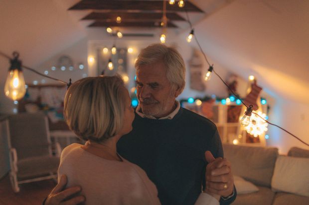 An elderly couple is dancing together in a living room.