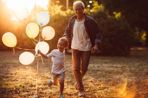 An elderly man and a young boy are running with balloons in a park.