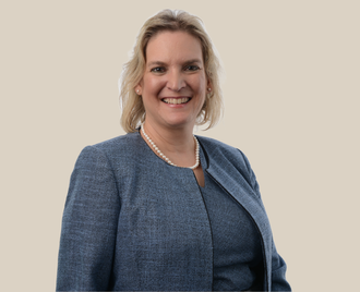A woman in a blue jacket and pearl necklace is smiling.