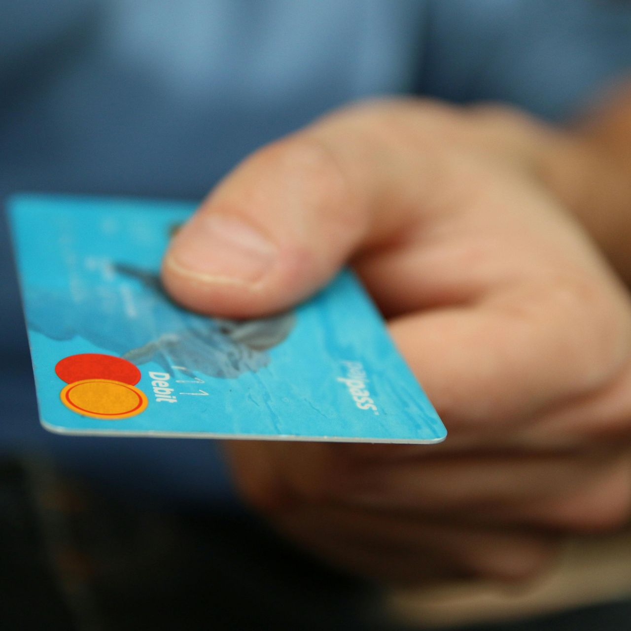 Hand holding a blue debit card with Mastercard logo.