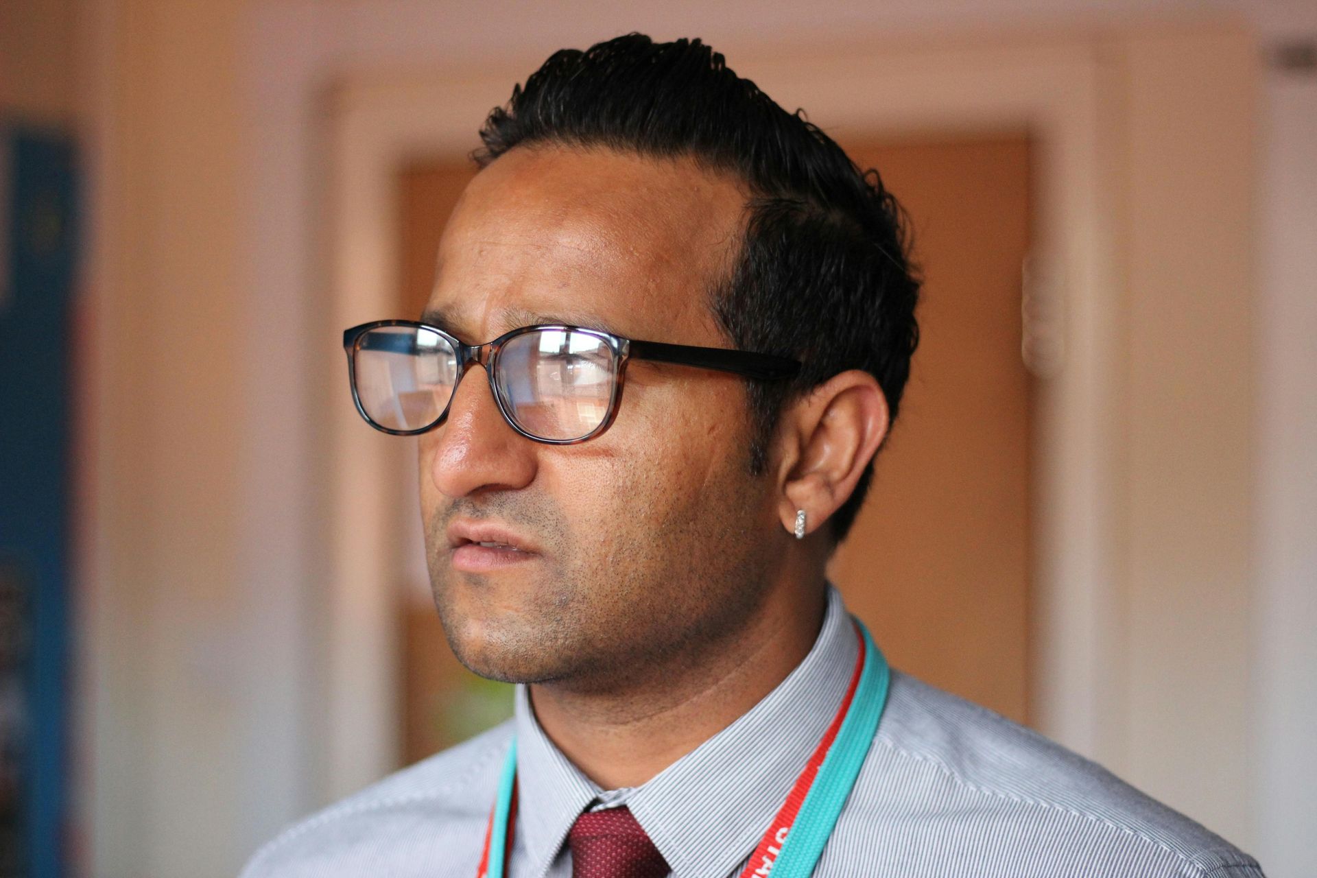 Man wearing glasses, looking to the side, wearing a shirt with a lanyard, indoors.