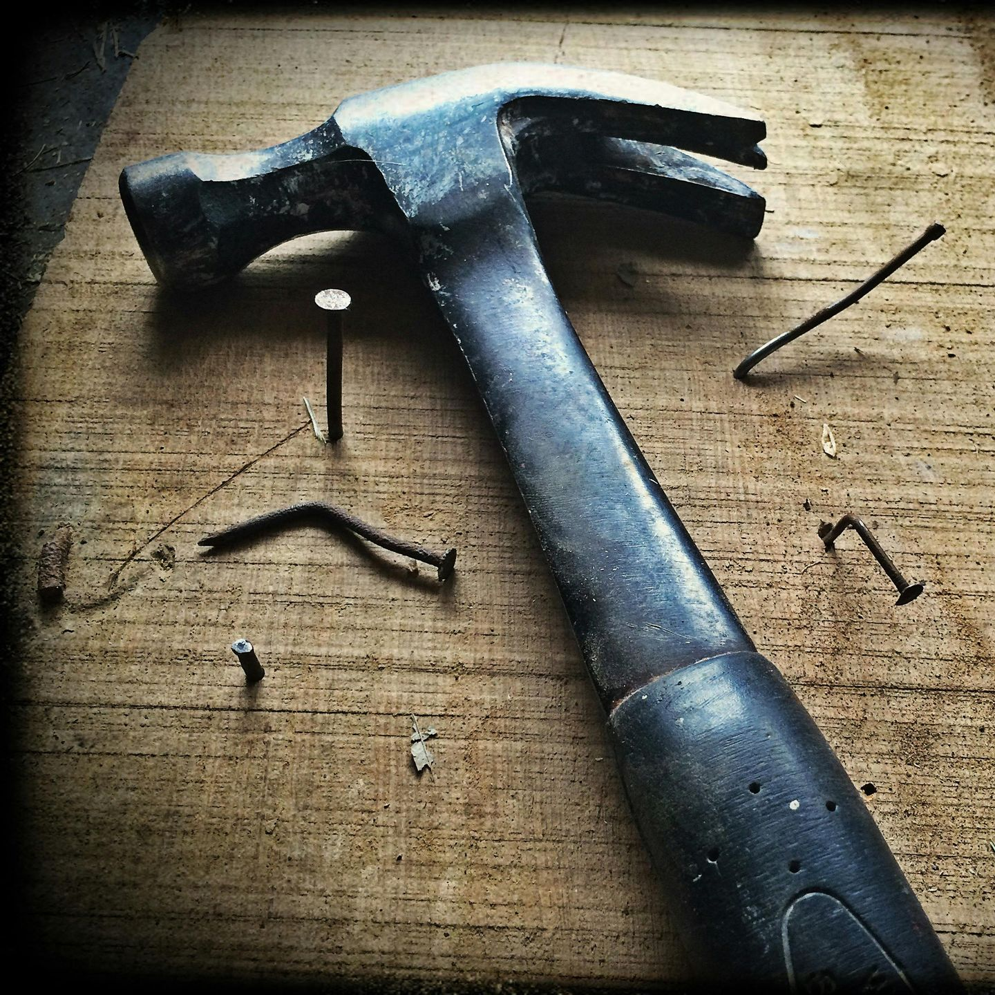 Hammer resting on a wood surface, surrounded by bent and loose nails.